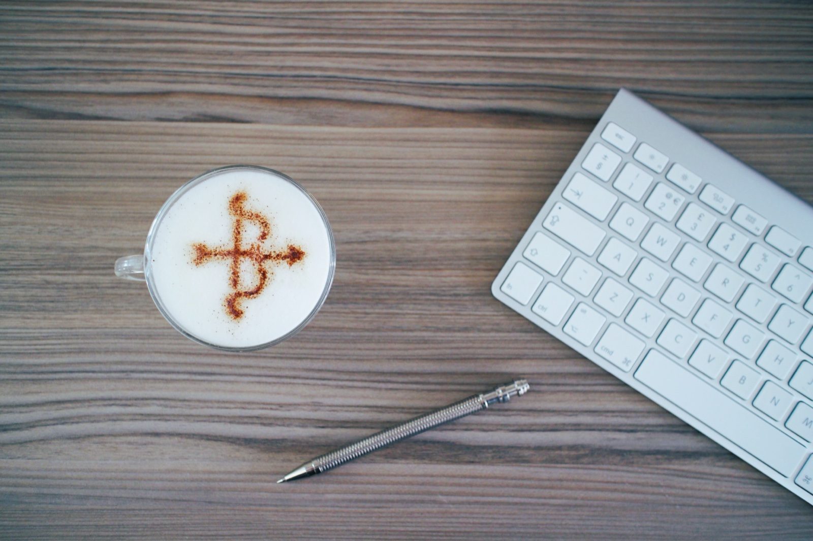 A cappuccino with the Barton Accountancy bow-and-arrow logo stencilled in cinnamon on the milk foam, sat on a wooden desk beside a keyboard and pen